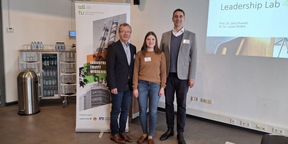 von links nach rechts: Prof. Dr. H. Holzmüller, Laura Wuttke und Prof. Dr. jens Rowold stehen vor dem Veranstaltungsplakat 